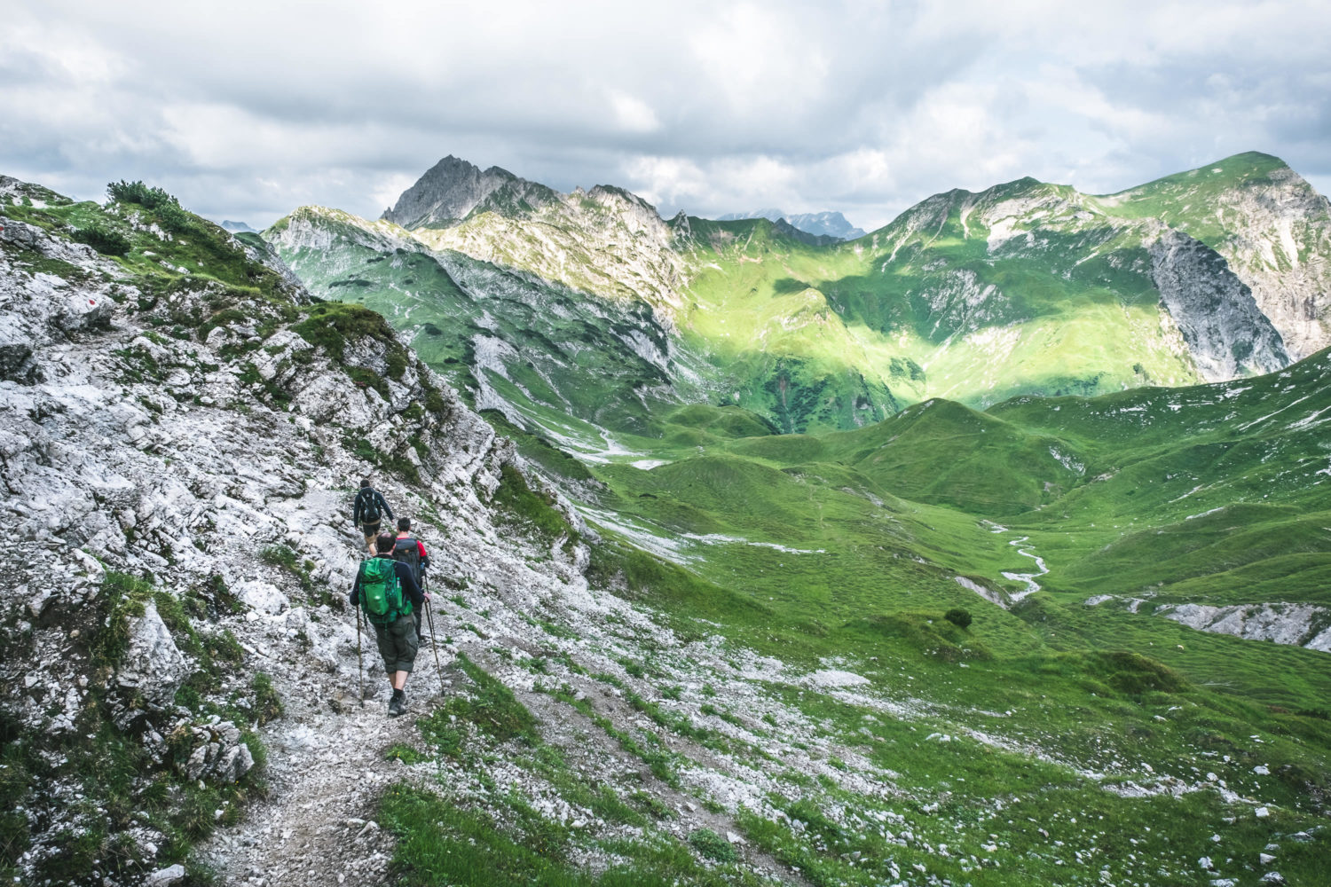 Drei Wanderer auf einem felsigen Pfad im Gebirge