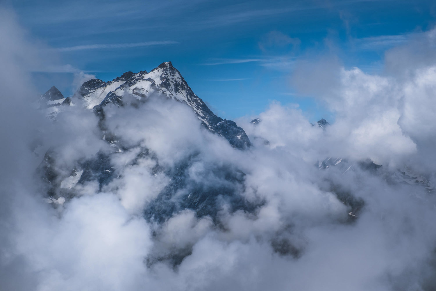 Berg mit schneebedeckten Hängen zwischen Wolken