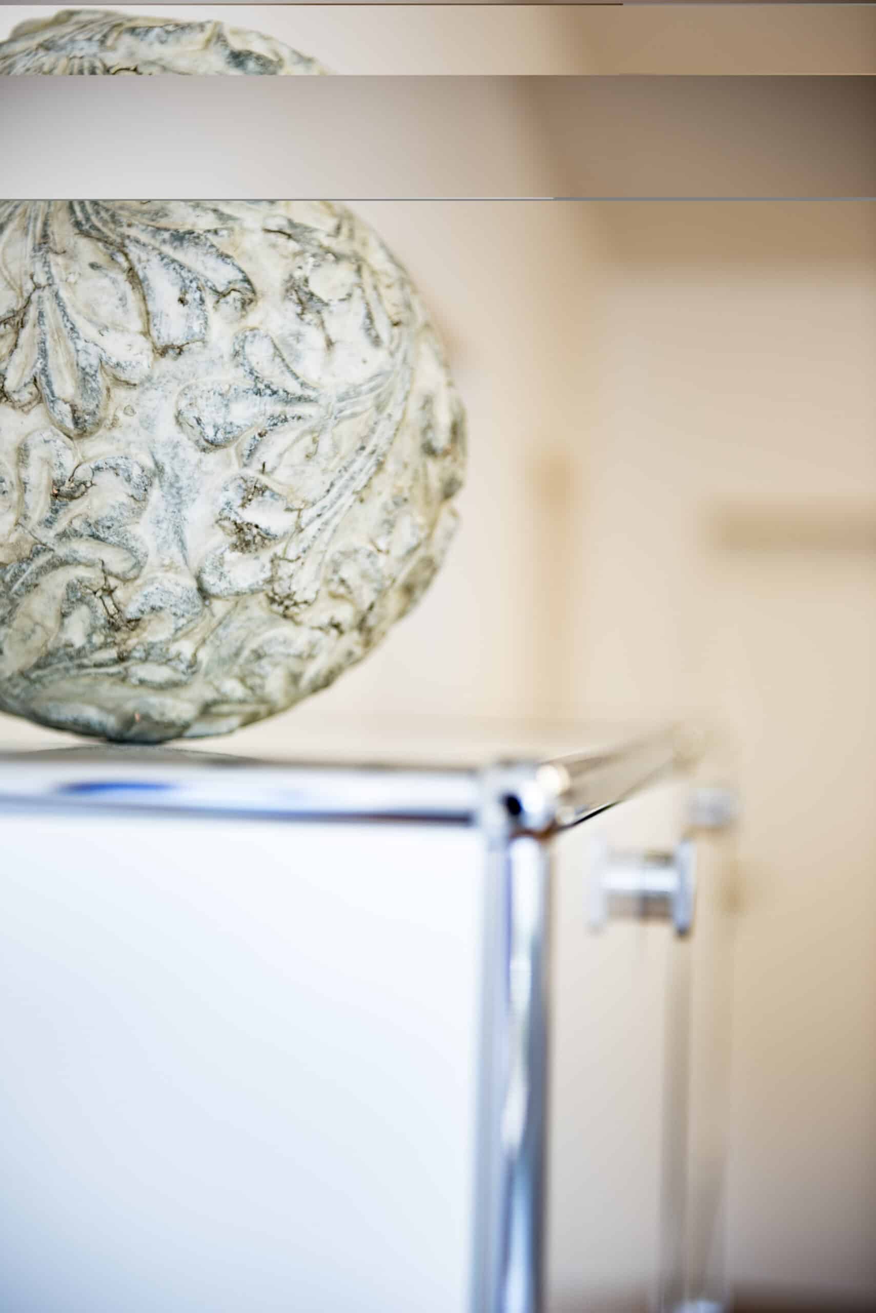 graue Kugel mit floralem Muster steht auf weißem Aktemschrank
