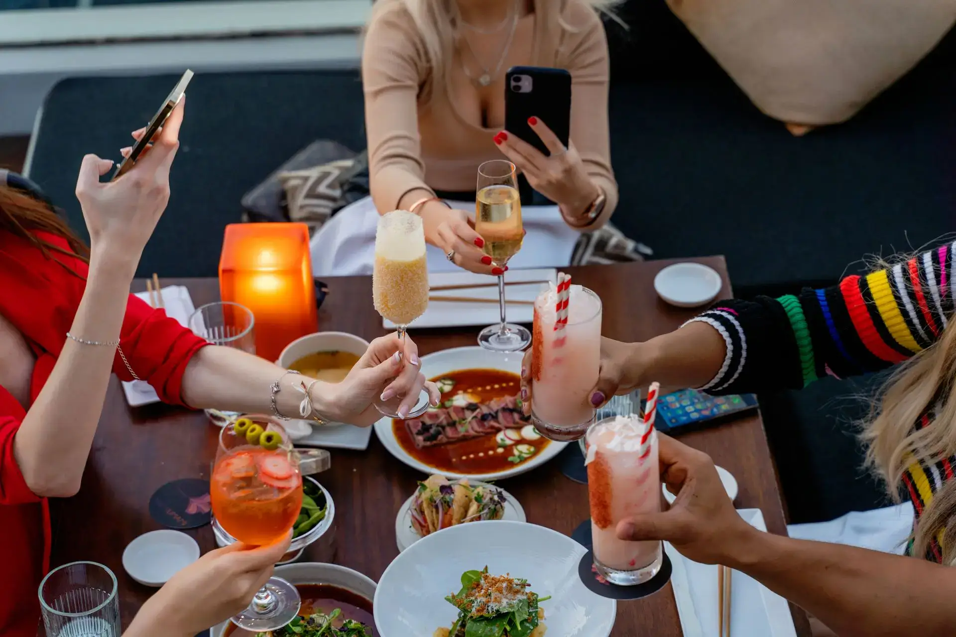 Group of friends toasting drinks over a shared meal at an outdoor restaurant table