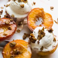 Caramelized peaches with ice cream and crumble on top on a marble surface.