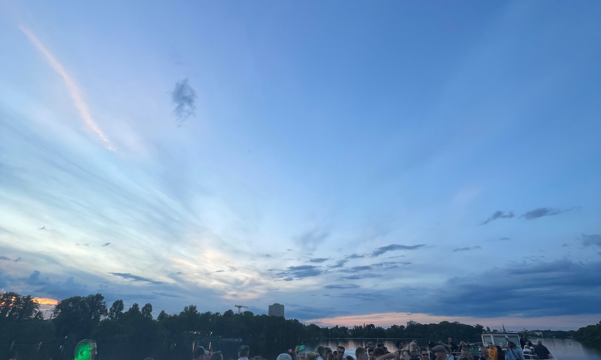Bootsparty Potsdam auf der Havel bei Sonnenuntergang: Gäste feiern und tanzen auf dem Oberdeck eines Schiffes vor der abendlichen Skyline von Potsdam.