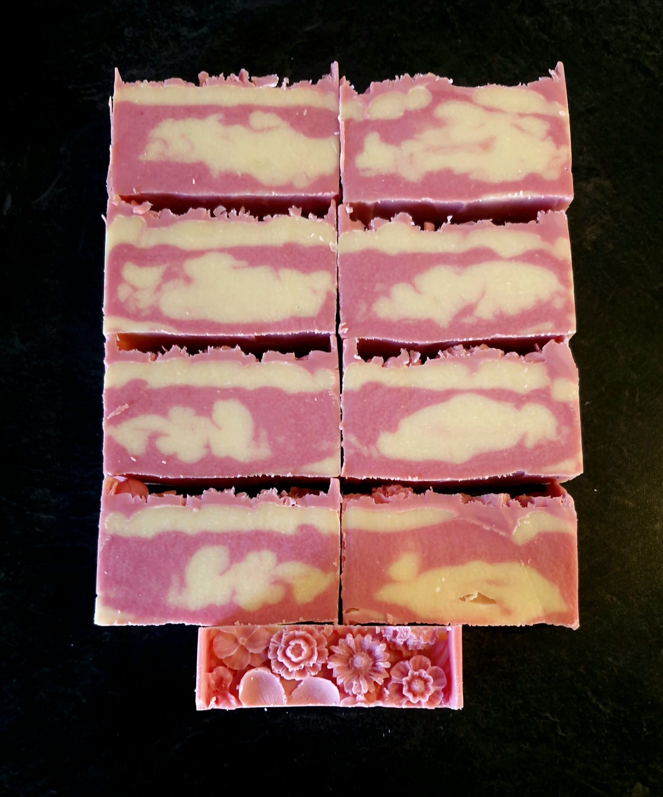 Sliced tallow soap bars showing a pink and cream swirl pattern, with a floral-molded top bar alongside, Fatglow soap art