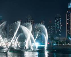 عرض نافورة دبي الموسيقية مع أضواء برج خليفة والمنطقة المحيطة ليلاً.