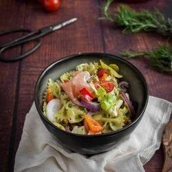 Italienischer Nudelsalat mit Pesto, frischem Gemüse, Mozzarella und luftgetrocknetem Schinken in einer großen weißen Schüssel – perfekt für den Grillabend.