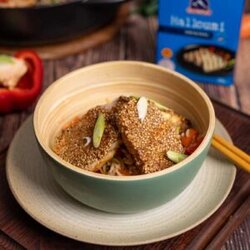 Goldbraun gebratener Halloumi mit knuspriger Sesamkruste, serviert auf einer bunten Reispfanne mit Paprika, Möhren und Frühlingszwiebeln.
