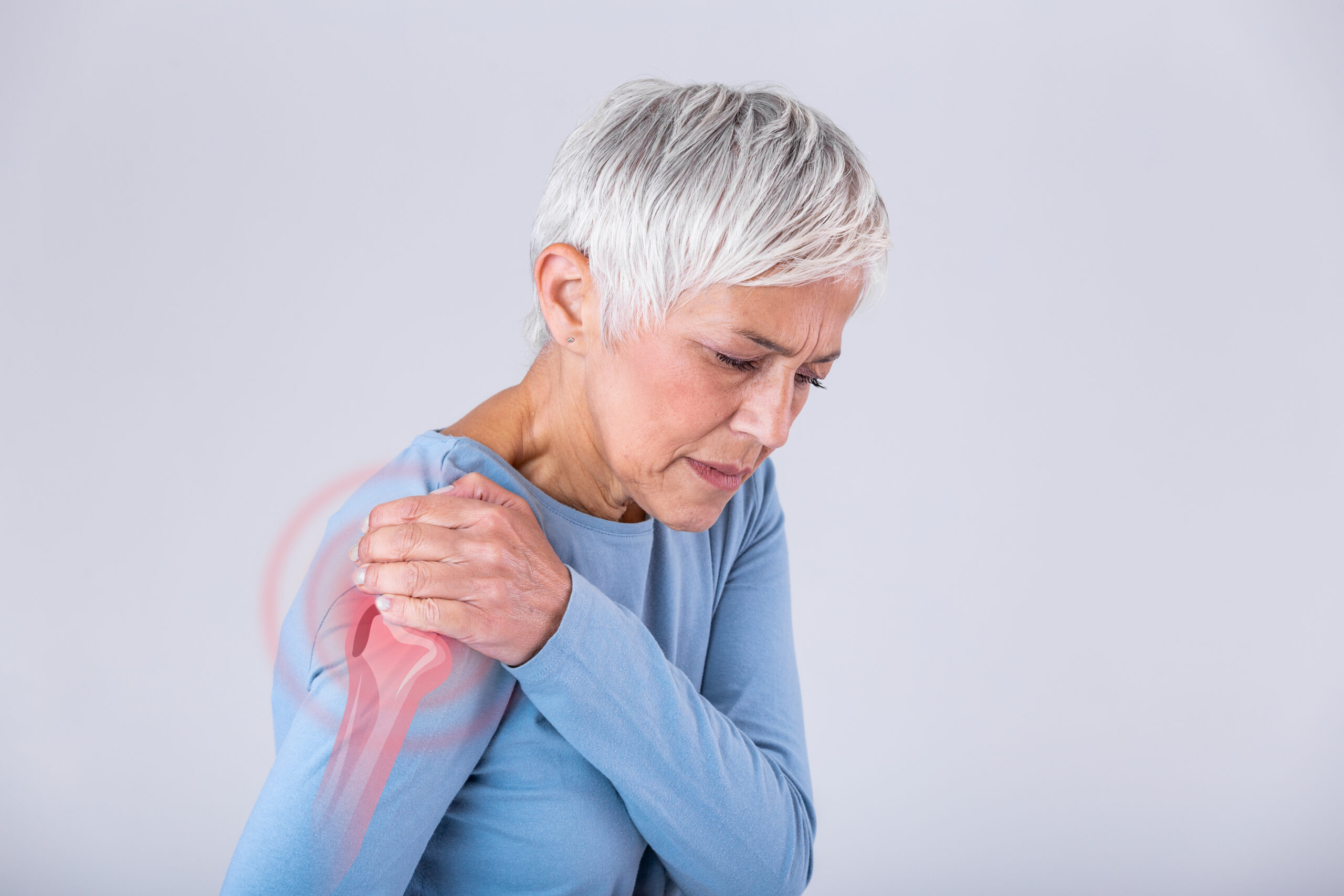Older woman wincing and holding her shoulder due to discomfort or chronic pain Older woman wincing and holding her shoulder due to discomfort or chronic pain