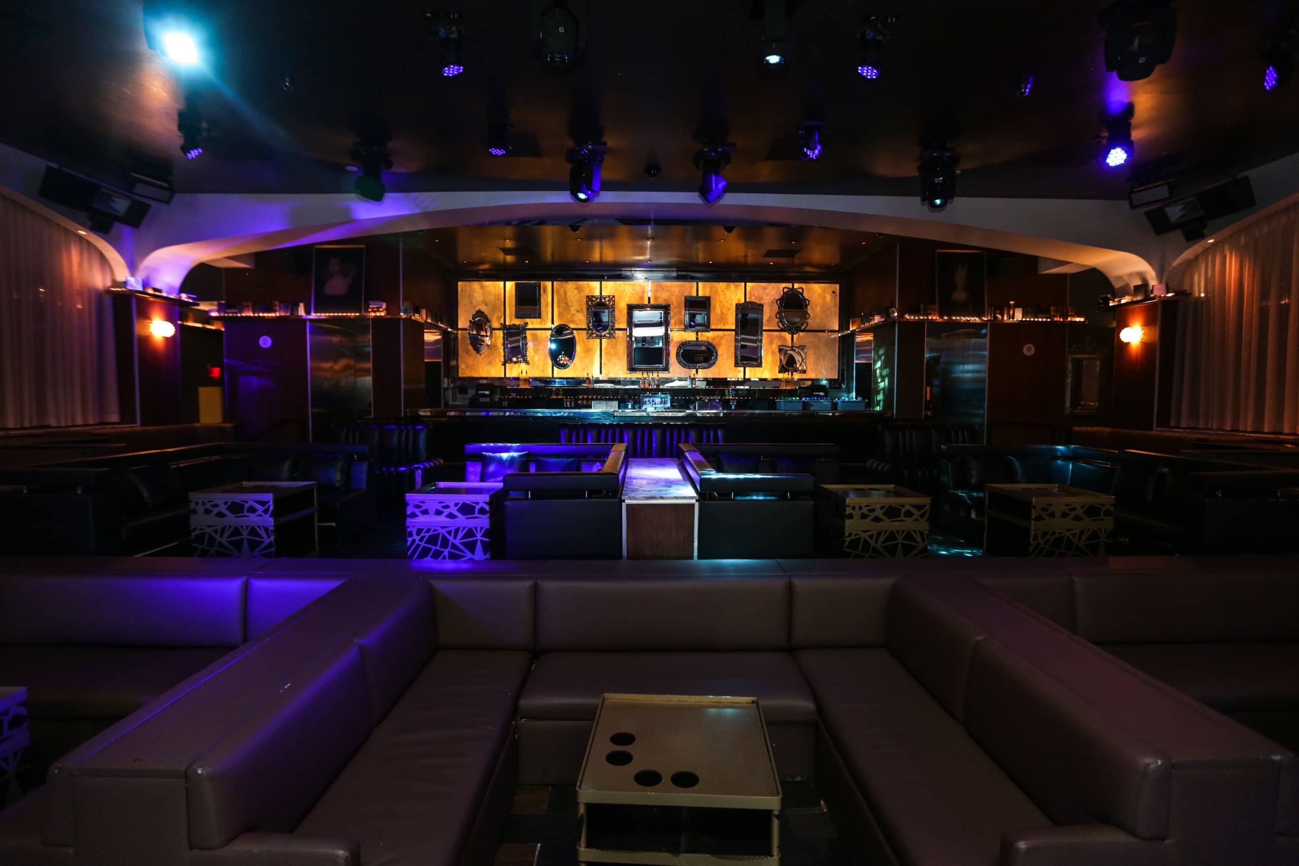 Dimly lit conference venue with purple lighting; lounge seating in the foreground and a stage in the back.