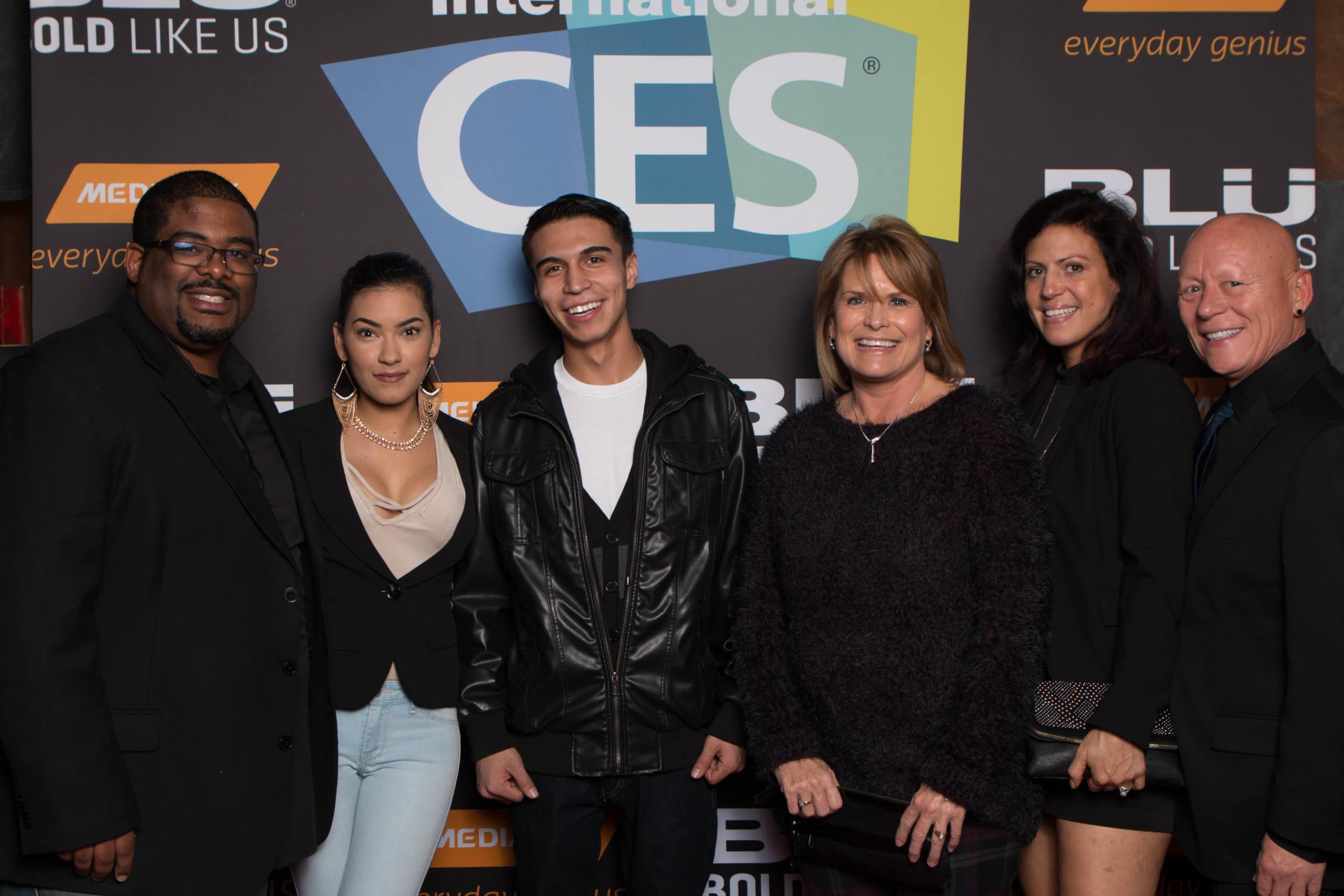 Group of six people smiling for a photo in front of a CES banner at a tech event.