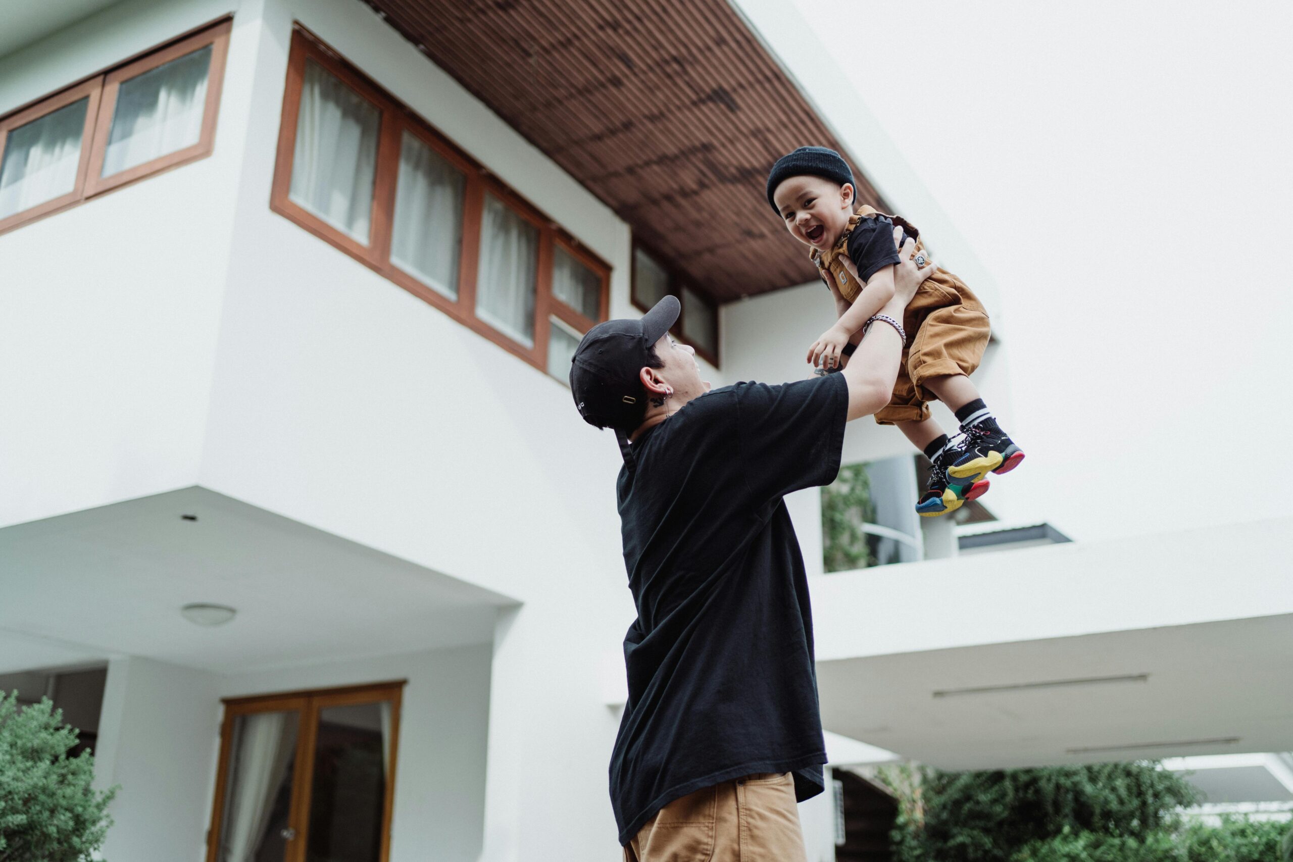 Père jouant avec son enfant devant une maison individuelle moderne - symbole de la qualité de vie et du quotidien d'une famille dans un foyer bien entretenu.