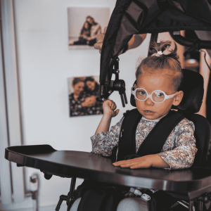 Close-up of Doris in her wheelchair with activity tray and sunshade fitted, looking directly at the camera