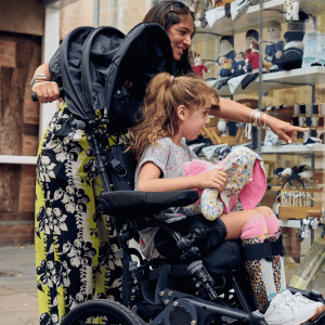 Lilac being pushed in her wheelchair by her mum while they look into a shop window in Hereford
