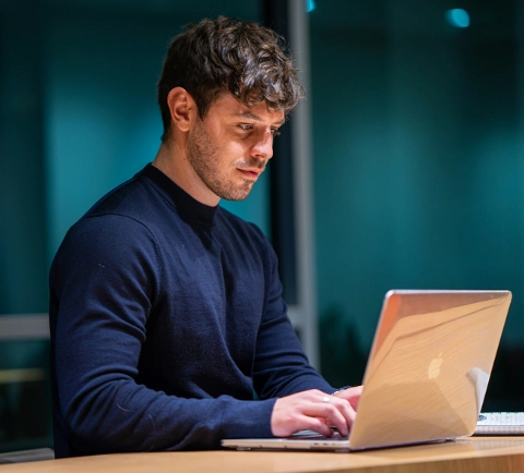 Focused man working late on a laptop in a modern office setting."
