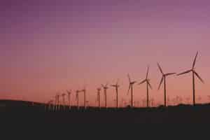 Row of wind turbines generating renewable energy at sunset with a purple and orange sky in the background.