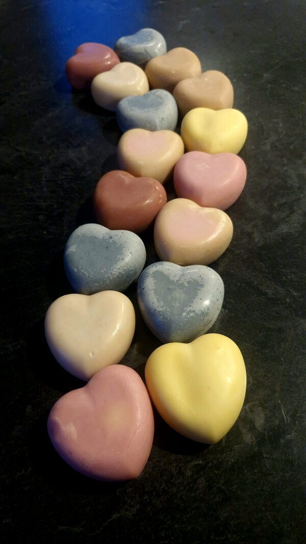 Two rows of grass-fed tallow heart soaps NZ in soft pastel shades — blush pink, grey, butter yellow, dusty rose and cream — arranged in a curved line, handmade by Fatglow