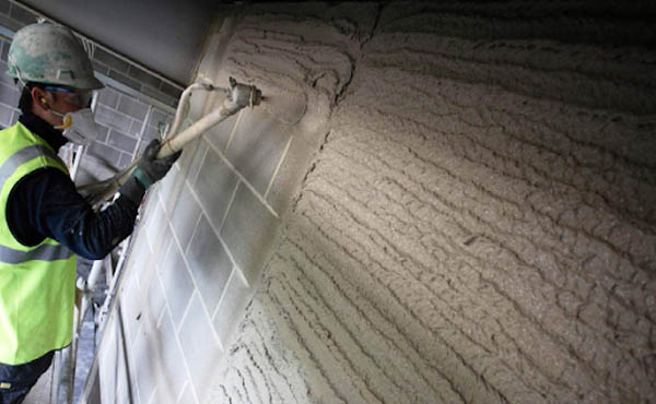 Worker applying cement plaster on wall using spray plastering machine