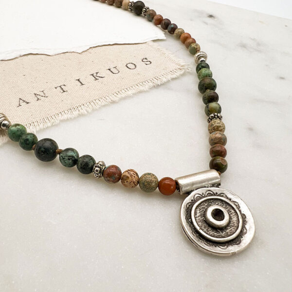 Beaded necklace with silver pendant on marble surface.