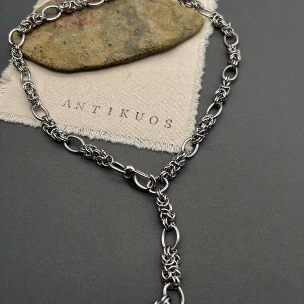 Silver chain necklace on fabric with ANTIKUOS logo.
