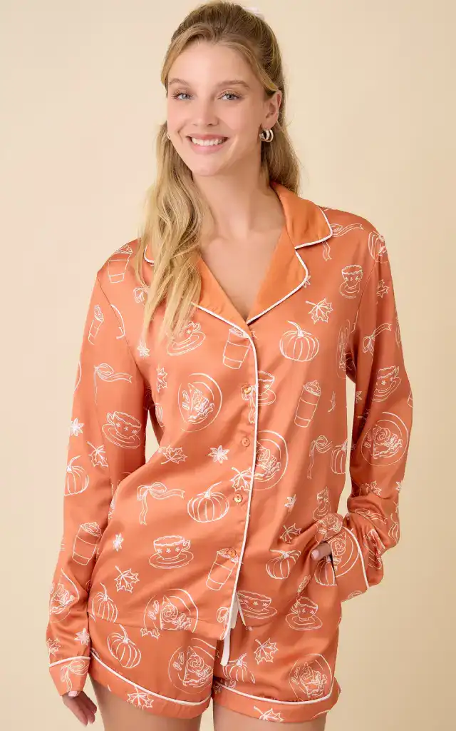 Luxurious burnt orange satin long-sleeve pajama set with elegant white pumpkin outline patterns, comfortable fit, perfect for solo self-care evenings and holiday lounging.