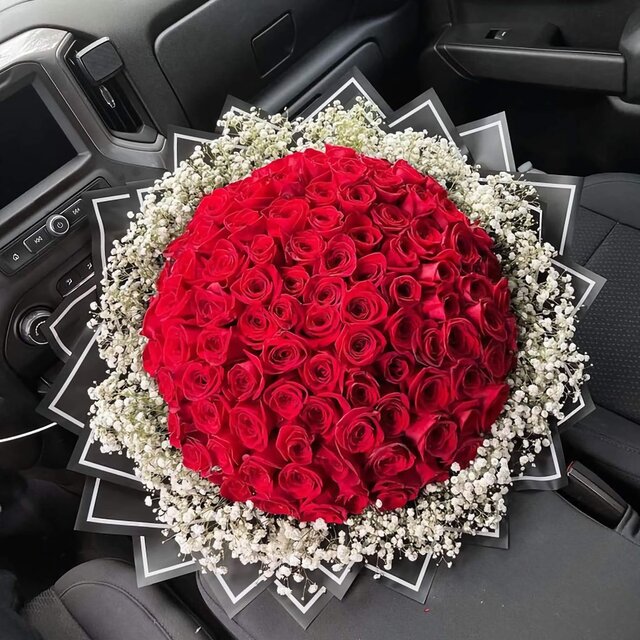 Luxurious bouquet of 100 fresh red roses surrounded by baby’s breath, wrapped in black paper, placed on a car seat – perfect for romantic flower delivery in Nairobi, Same Day Flower Delivery
