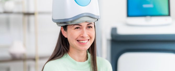 Smiling patient seated comfortably during a TMS therapy session with a helmet-style H coil