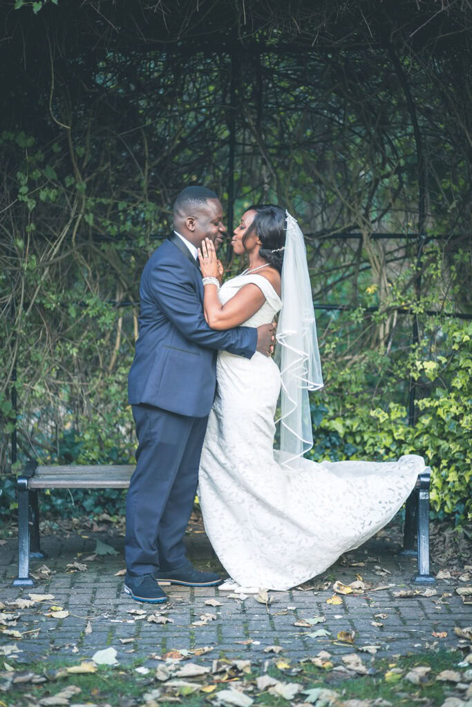 Happy couple kissing in a picturesque green garden alcove on their wedding day in South England