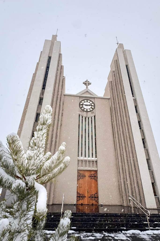 Snow-covered church with tall twin towers and a clock, set against a snowy sky.