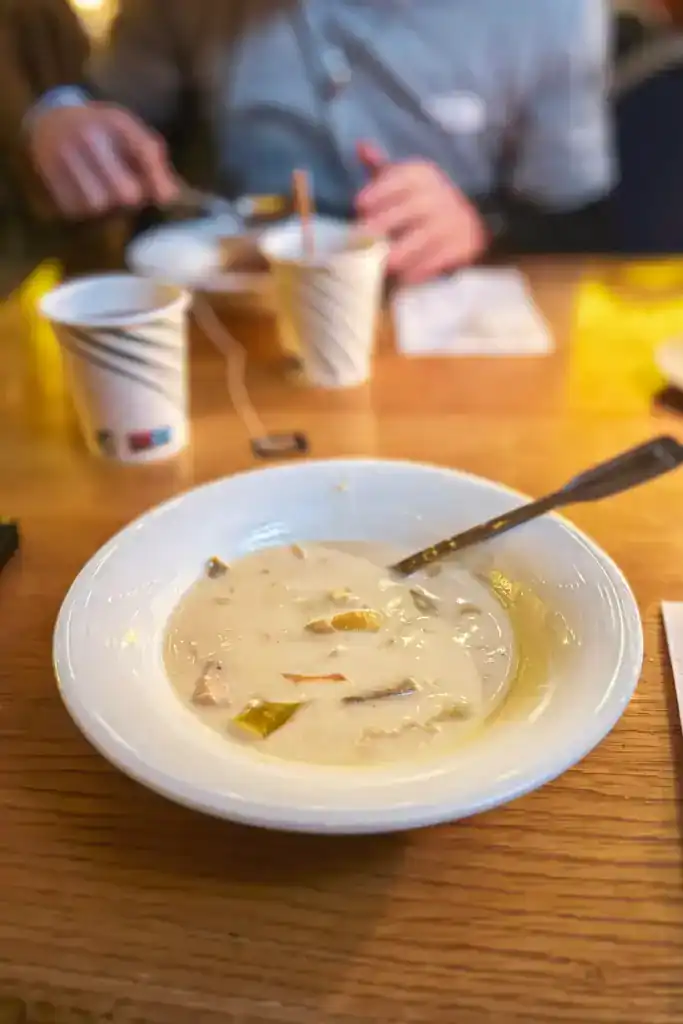 A bowl of creamy soup with vegetables and meat on a wooden table in a restaurant.