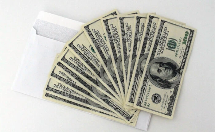 Mehrere 100-Dollar-Scheine fächerförmig auf einem weißen Umschlag ausgelegt.