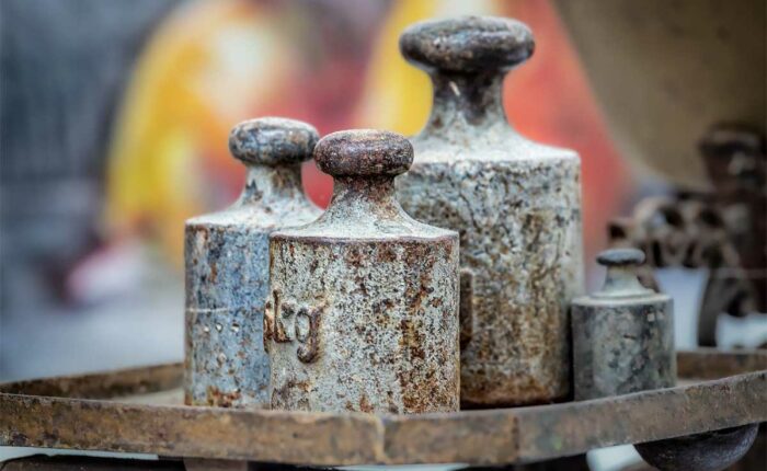 Mehrere alte, rostige Metallgewichte auf einer mechanischen Waage.