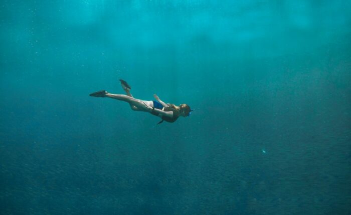 Frau mit Schnorchel schwimmt unter Wasser im offenen Meer.