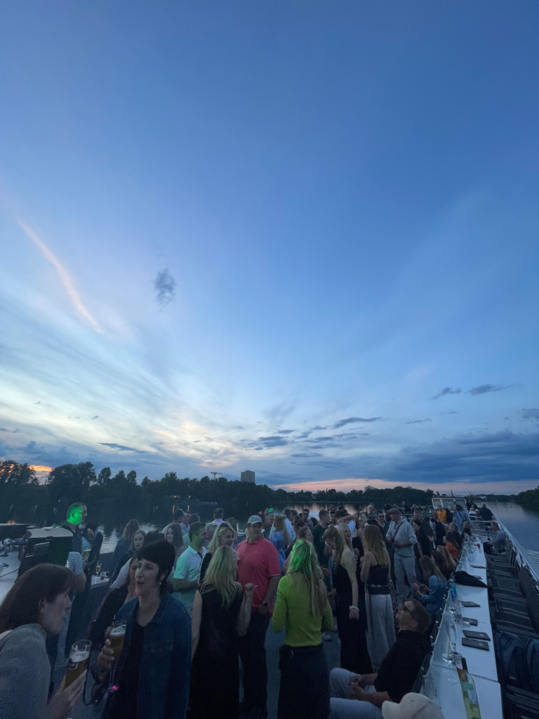 Bootsparty Potsdam auf der Havel bei Sonnenuntergang: Gäste feiern und tanzen auf dem Oberdeck eines Schiffes vor der abendlichen Skyline von Potsdam.