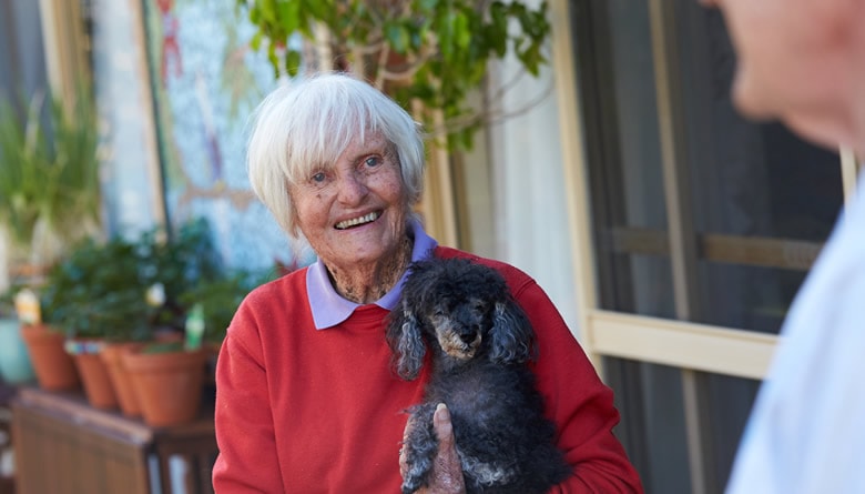 An elderly lady living with dementia holding a small black dog