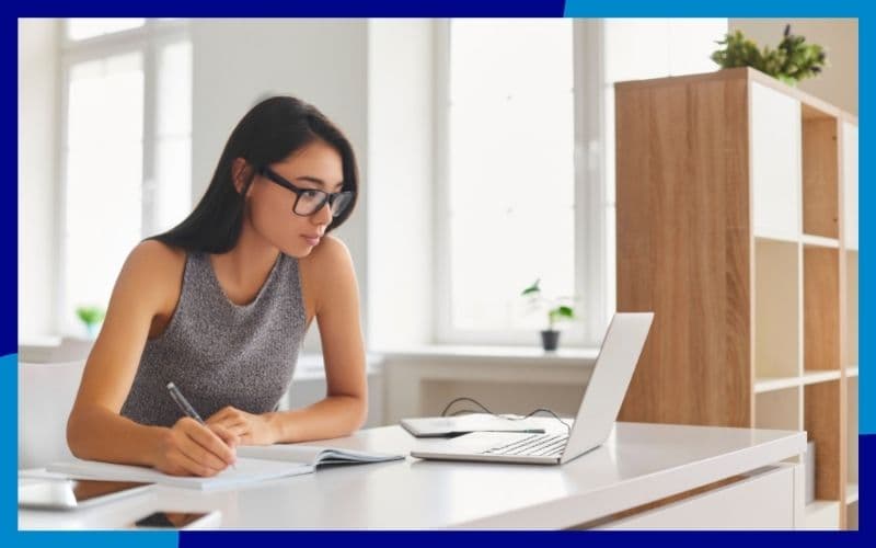 Ragazza seduta alla scrivania davanti al pc che prende appunti