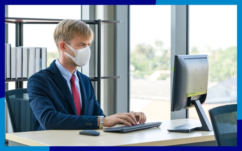 Uomo con la mascherina che lavora al computer nel suo ufficio