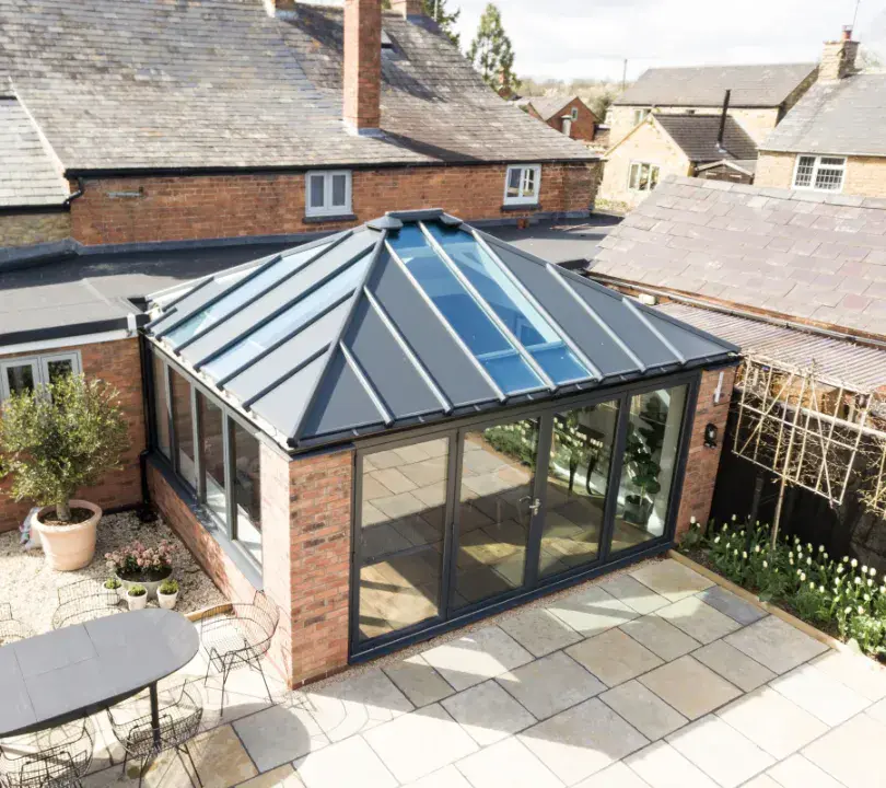 Brick conservatory extension with a dark solid roof, roof light and wide garden-facing doors.