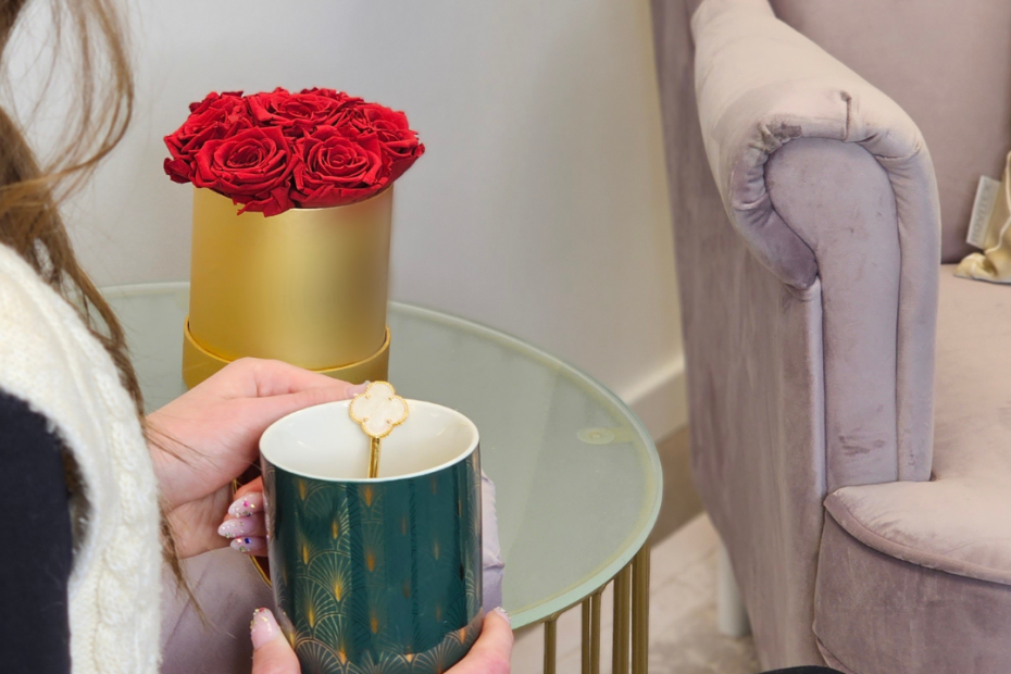 A képen egy fiatal mő és púder színű fotel található. Az asztalon rózsa arany dobozban, arany asztalon.