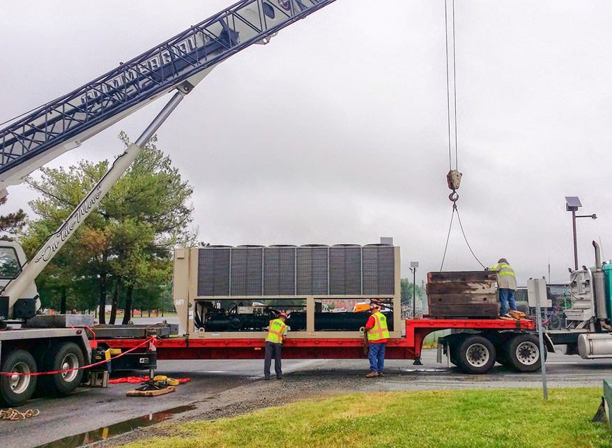 Workers unload a large container from a truck using a crane.