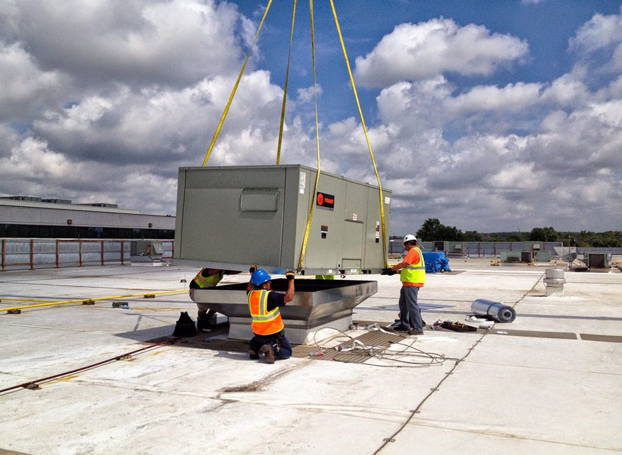 Workers installing a large generator on a rooftop.