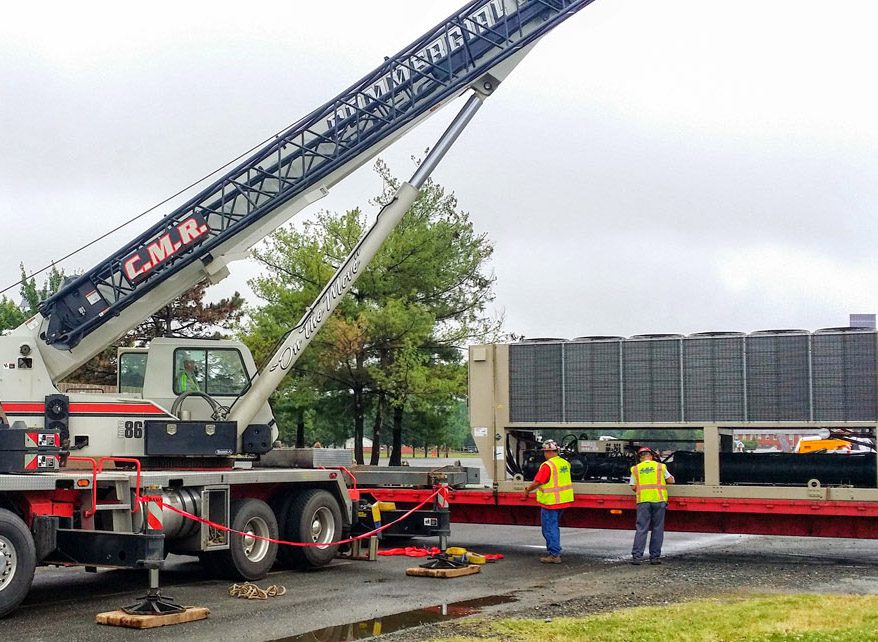 Workers operate a crane truck on a construction site under cloudy skies.