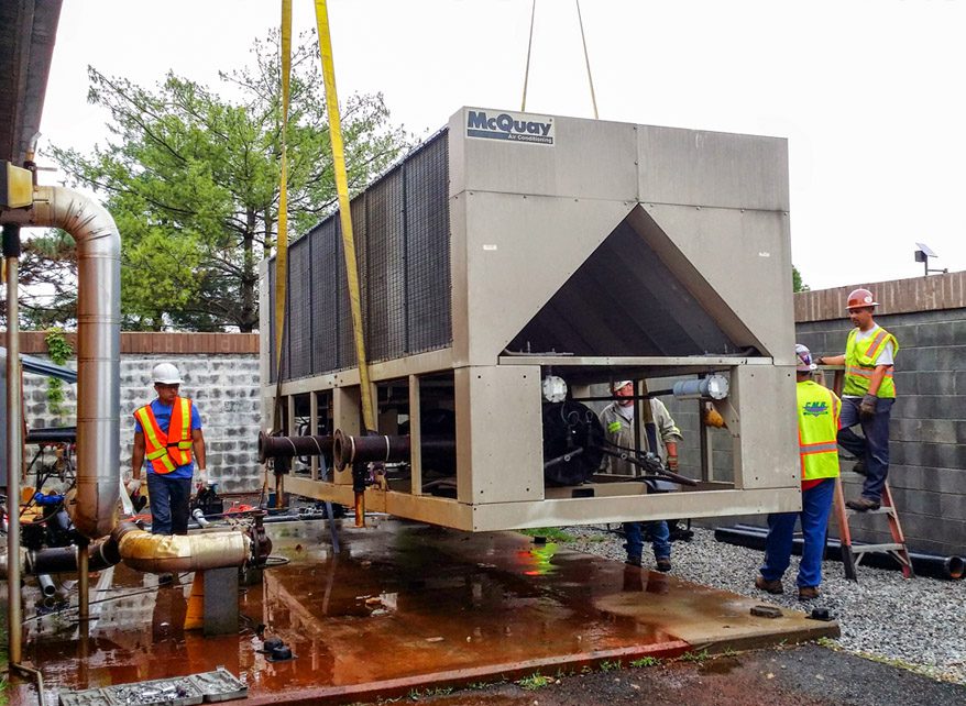 Workers installing a large McQuay HVAC unit outdoors.
