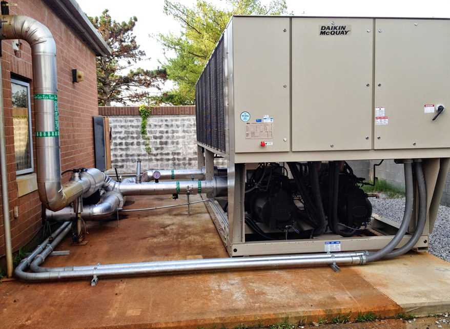 Industrial HVAC unit installed outdoors on a concrete platform beside a brick building.