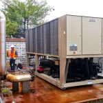 Thumbnail of http://Technician%20inspecting%20large%20industrial%20HVAC%20unit%20outdoors%20on%20rainy%20day.