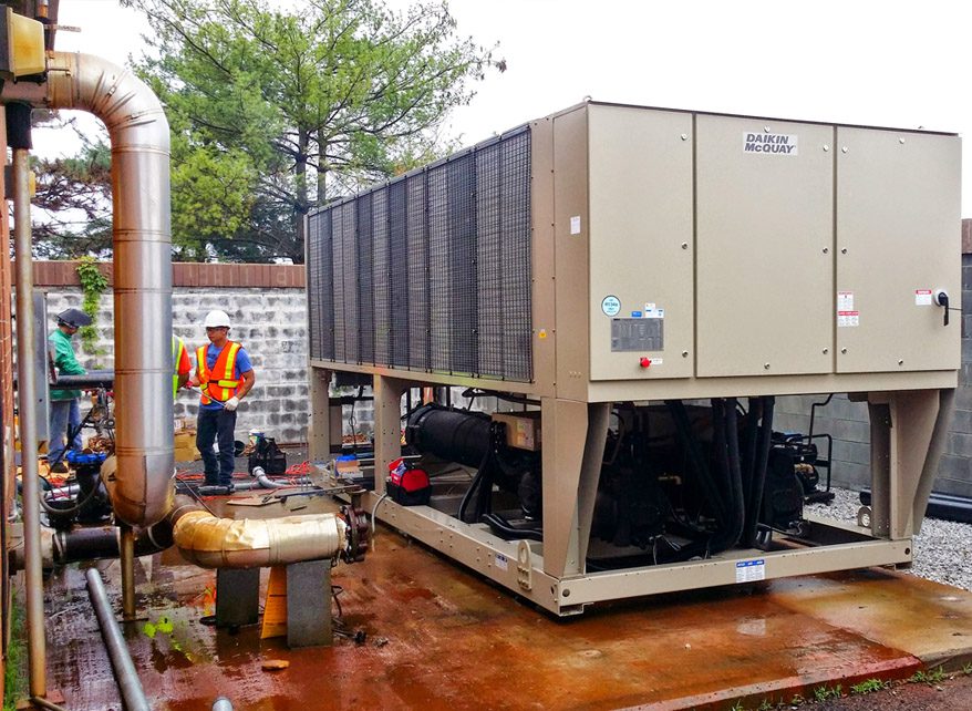 Technician inspecting large industrial HVAC unit outdoors on rainy day.