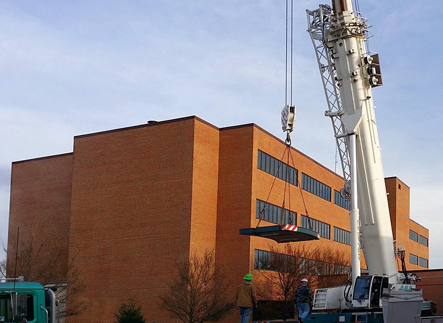 Crane lifting a heavy object beside a brick building.