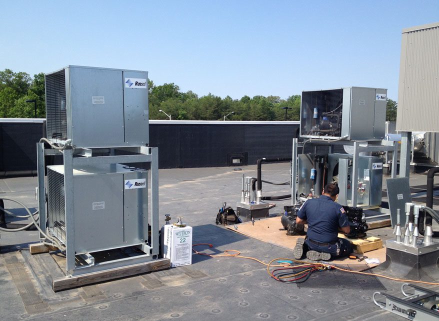Technicians installing HVAC units on a rooftop under clear skies.