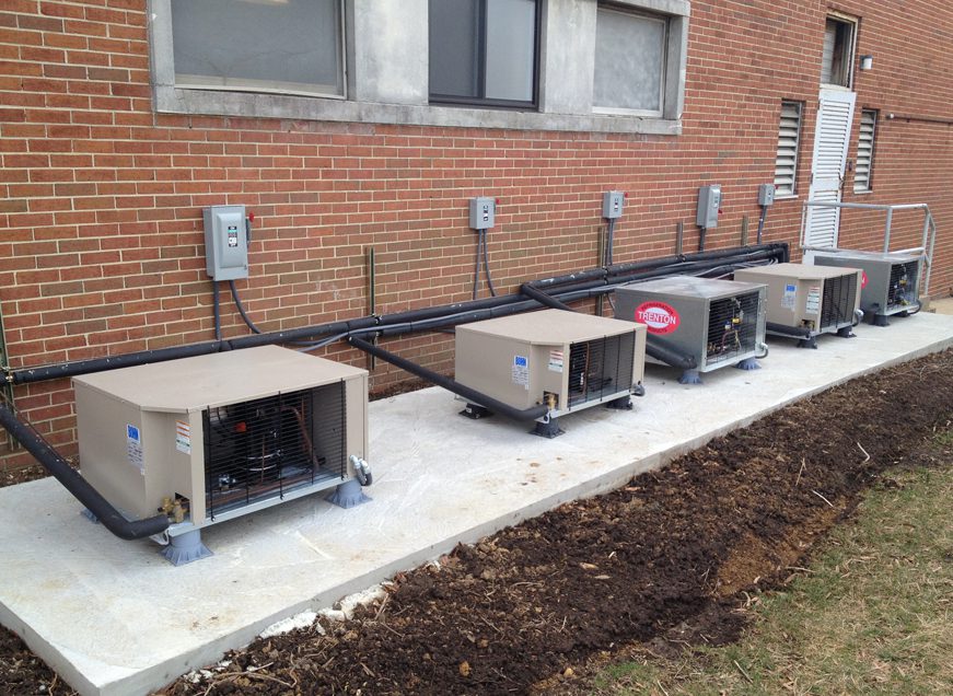 Row of outdoor HVAC units installed against a brick building.