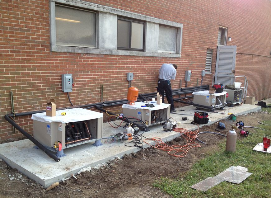 Technician working on HVAC units outside a brick building.