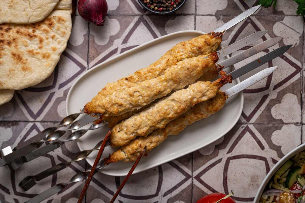 Nahaufnahme eines Hähnchen Kebab Spießes mit geprägten Fingerkerben, typisch für Koobideh