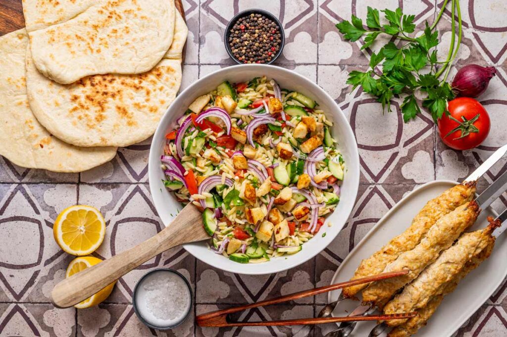 Mediterraner Kritharaki Salat mit gebratenem Halloumi, Petersilie und frischem Gemüse, serviert in einer Schale